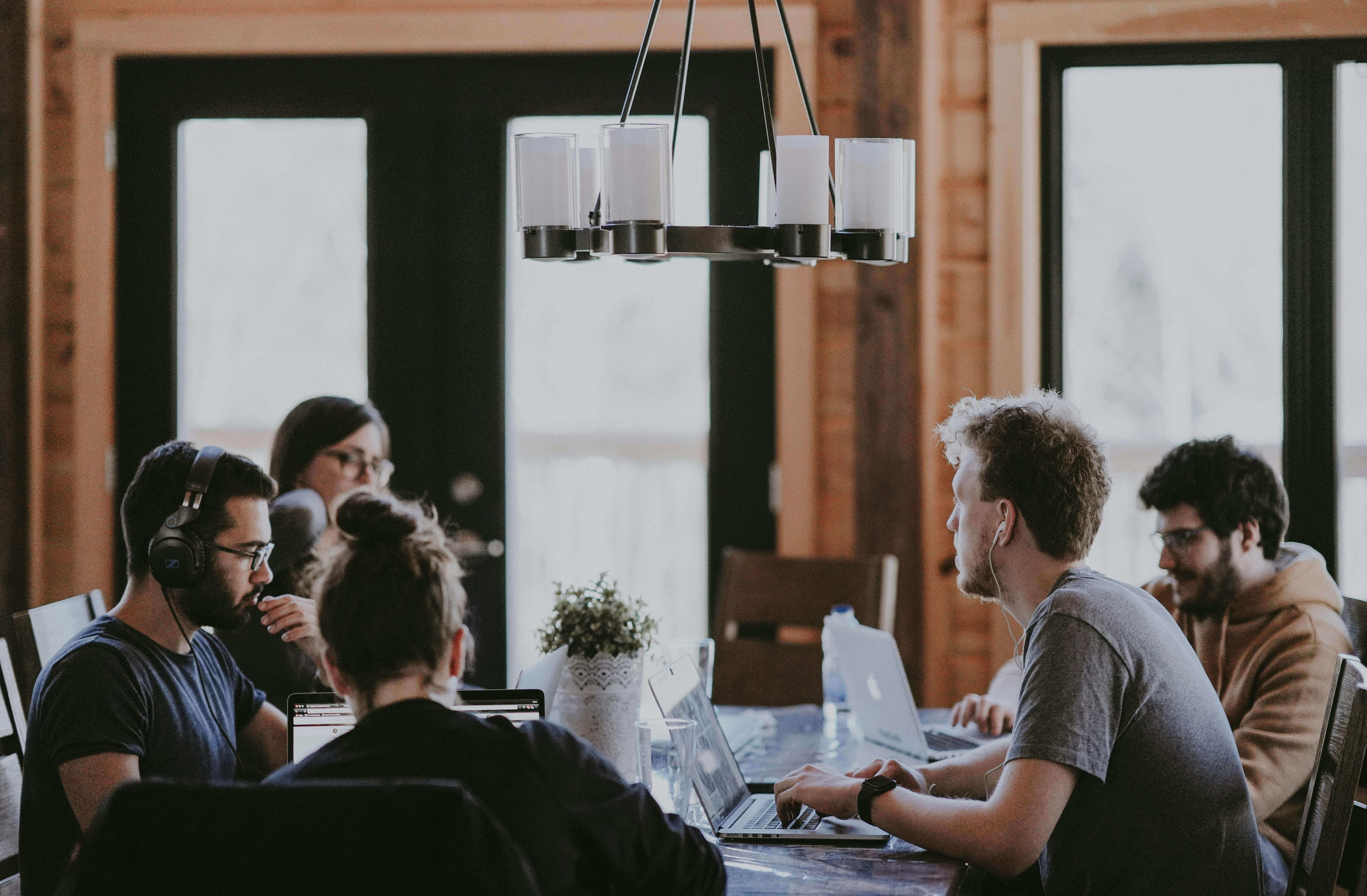 A group of young professionals working together on laptops around a wooden conference table in a rustic office setting