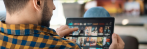 Man with plaid shirt browses Netflix on a tablet, showing movie thumbnails