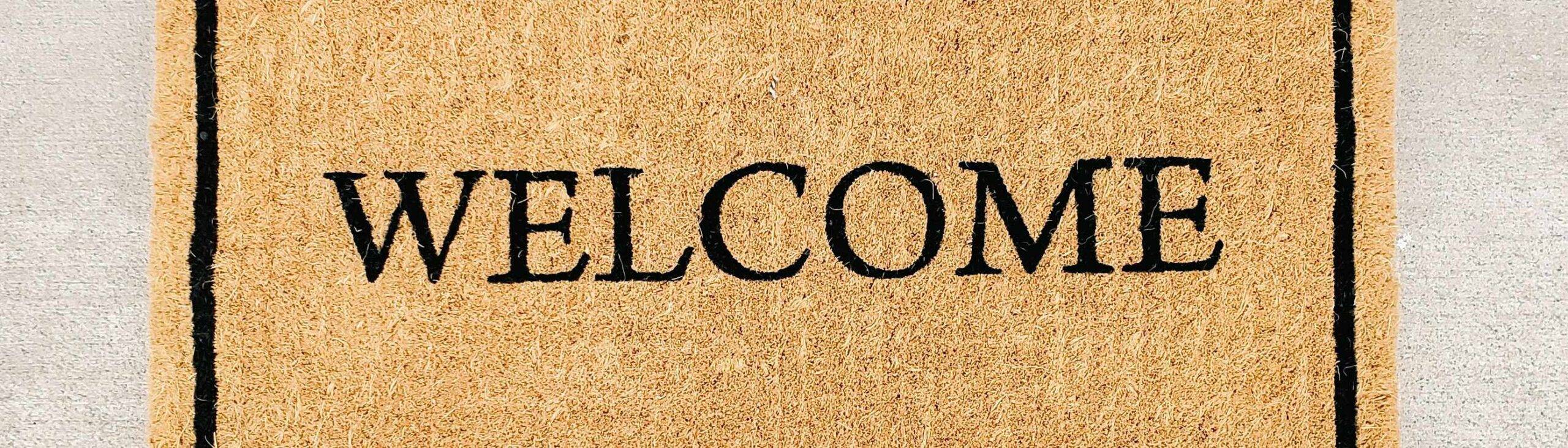 Person's point of view looking down at their shoes in from of a welcome mat