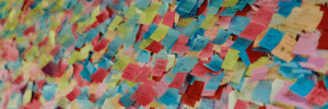 Colorful wall covered with numerous handwritten sticky notes in blue, pink, yellow, and red tones, forming a dense collage of messages and names at what appears to be an event or exhibition space.